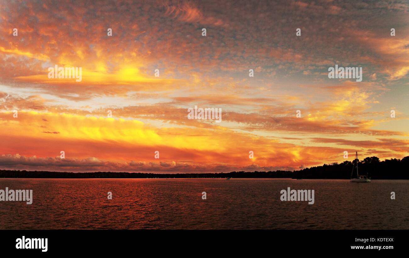 Un llamativo color dorado de inspiración nublado atardecer lago de agua salada con agua reflexiones. capturados en el lago Macquarie, Australia. Foto de stock