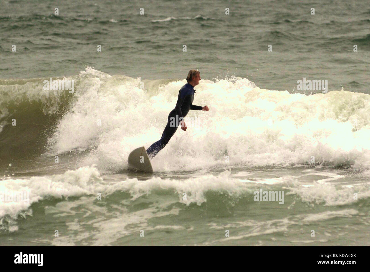 Surfer en un traje húmedo en invierno montando una onda y a punto de caer en el mar en Boscombe, Bournemouth, Dorset, Reino Unido. Foto de stock