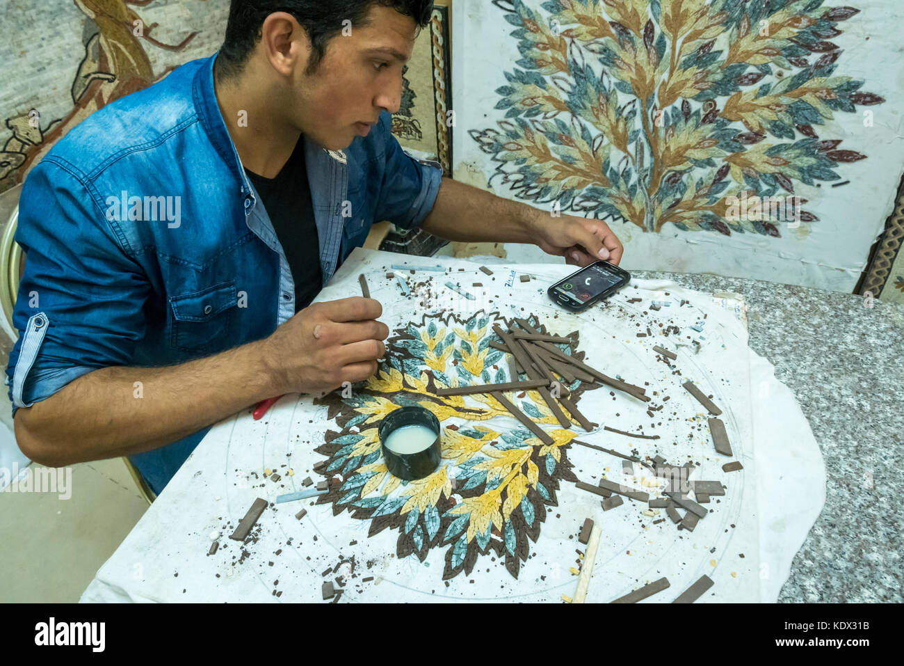 Árbol de vida intrincado trabajo de mosaico, mosaico de Madaba y taller de artesanías, con el joven hombre controlar su teléfono móvil, Jordania, Oriente Medio Foto de stock