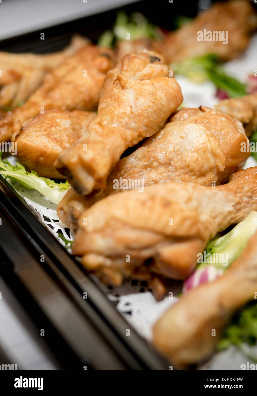 Cerca de palillos de tambor de pollo asado en un buffet en una bandeja negra con lechuga como guarnición Foto de stock