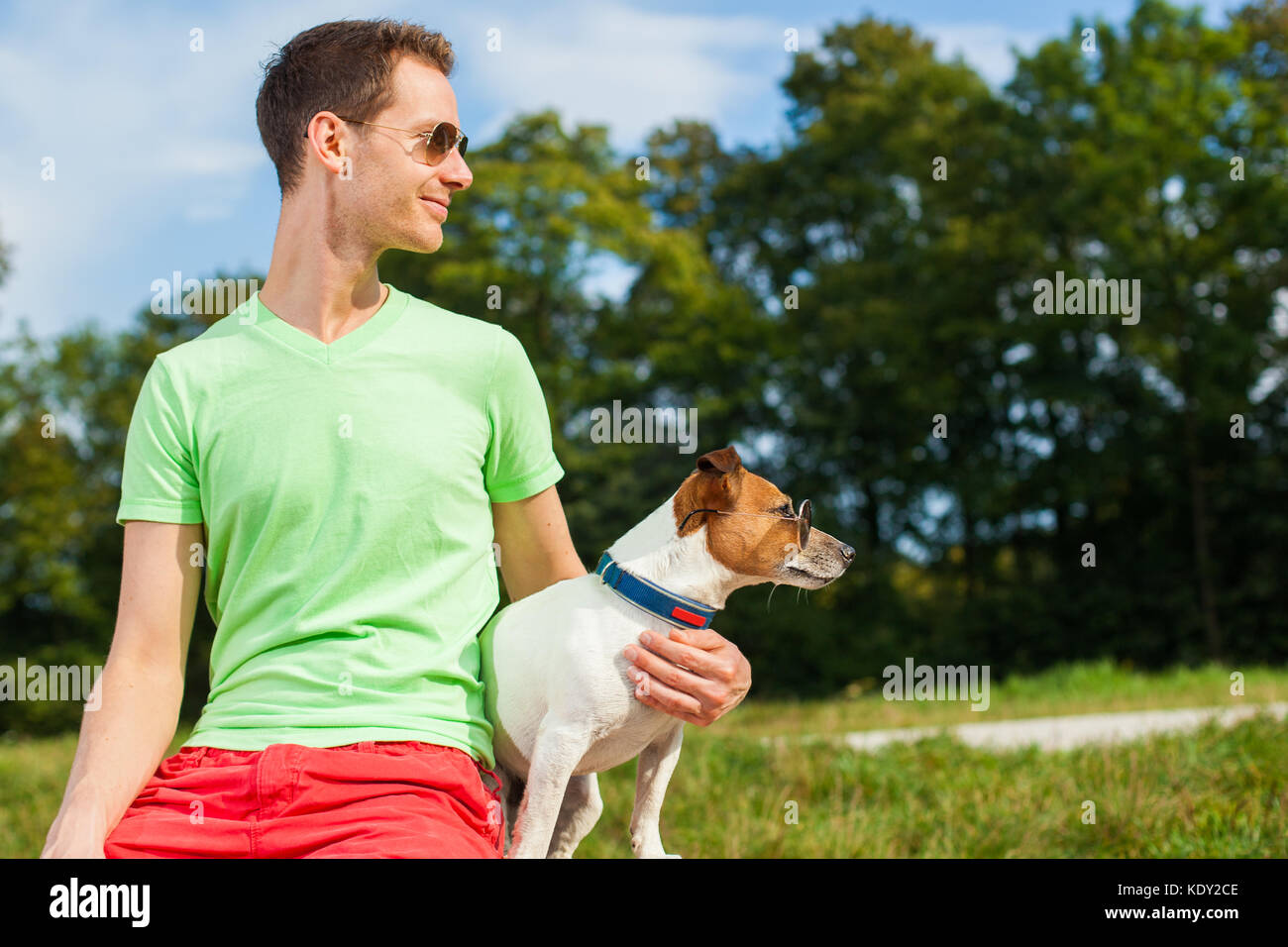 Perro y dueño observando juntos, sentados muy cerca, junto con un buen tiempo al aire libre Foto de stock