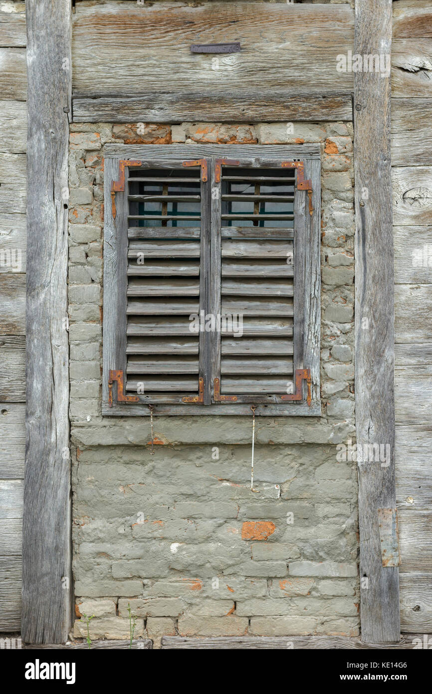 Ventana de madera antigua con persianas de madera en una casa de madera abandonada Foto de stock