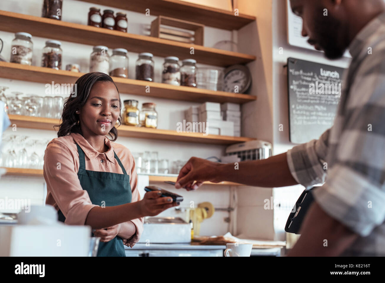 El cliente usando una tarjeta bancaria y tecnología nfs para pagar un barista para una compra en una cafetería Foto de stock