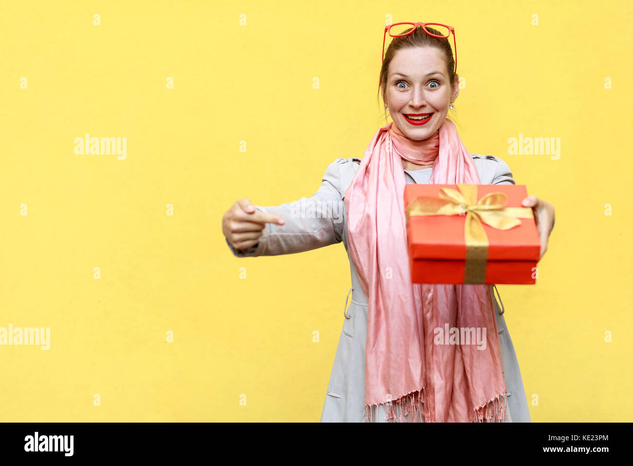 Mujer adulta joven dedo señalador en caja de regalo y mirando a la cámara y gran sonrisa. sobre fondo amarillo. Foto de estudio Foto de stock
