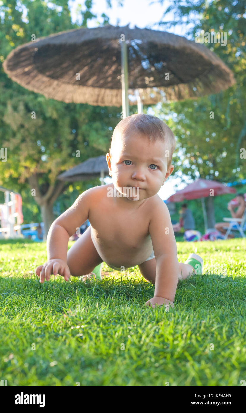 niño de 1 años arrastrándose en el césped de la piscina. Desarrollo de habilidades motoras Foto de stock