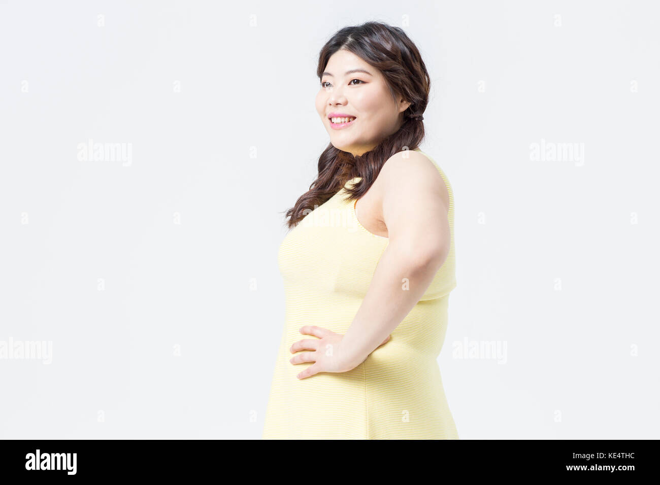 Vista lateral de la grasa en la mujer joven sonriente vestido amarillo posando Foto de stock