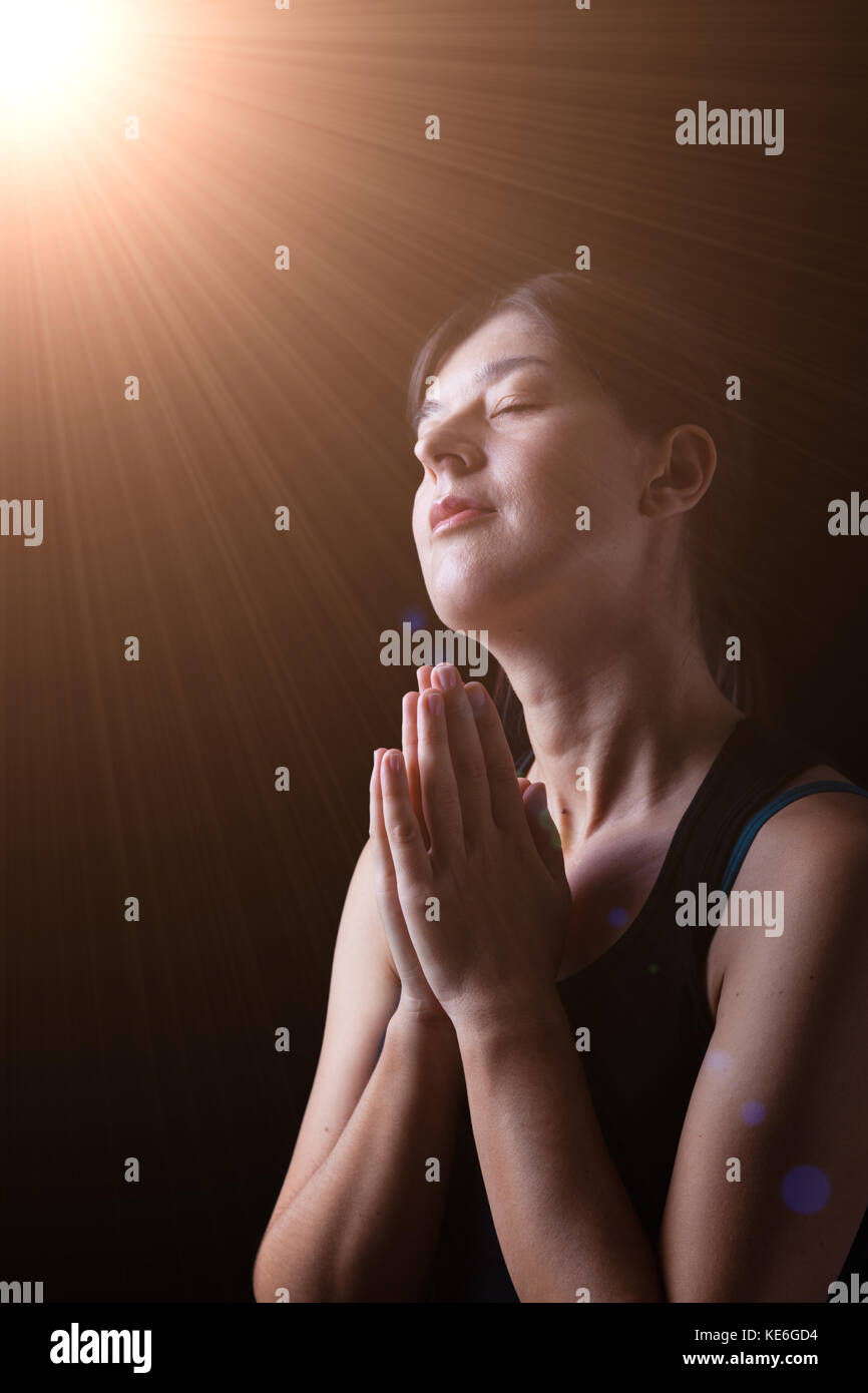 Mujer fiel orando y sonriente en la felicidad, gozo y paz, bajo una luz celestial divino o sentirse inspirados con la presencia de Dios Foto de stock