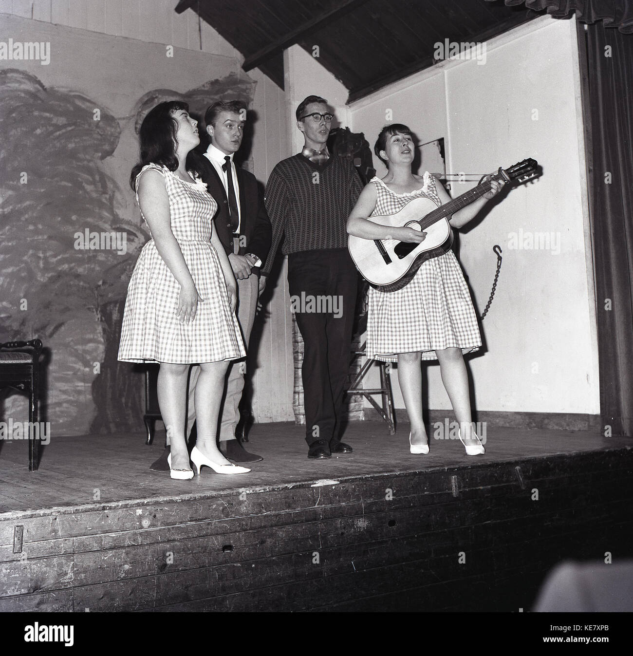 1960, histórico, cuatro adultos jóvenes cantantes masculinos y femeninos, uno con la guitarra, en el escenario del barrio Assembley Hall, Aylesbury, Bucks, Inglaterra. Foto de stock