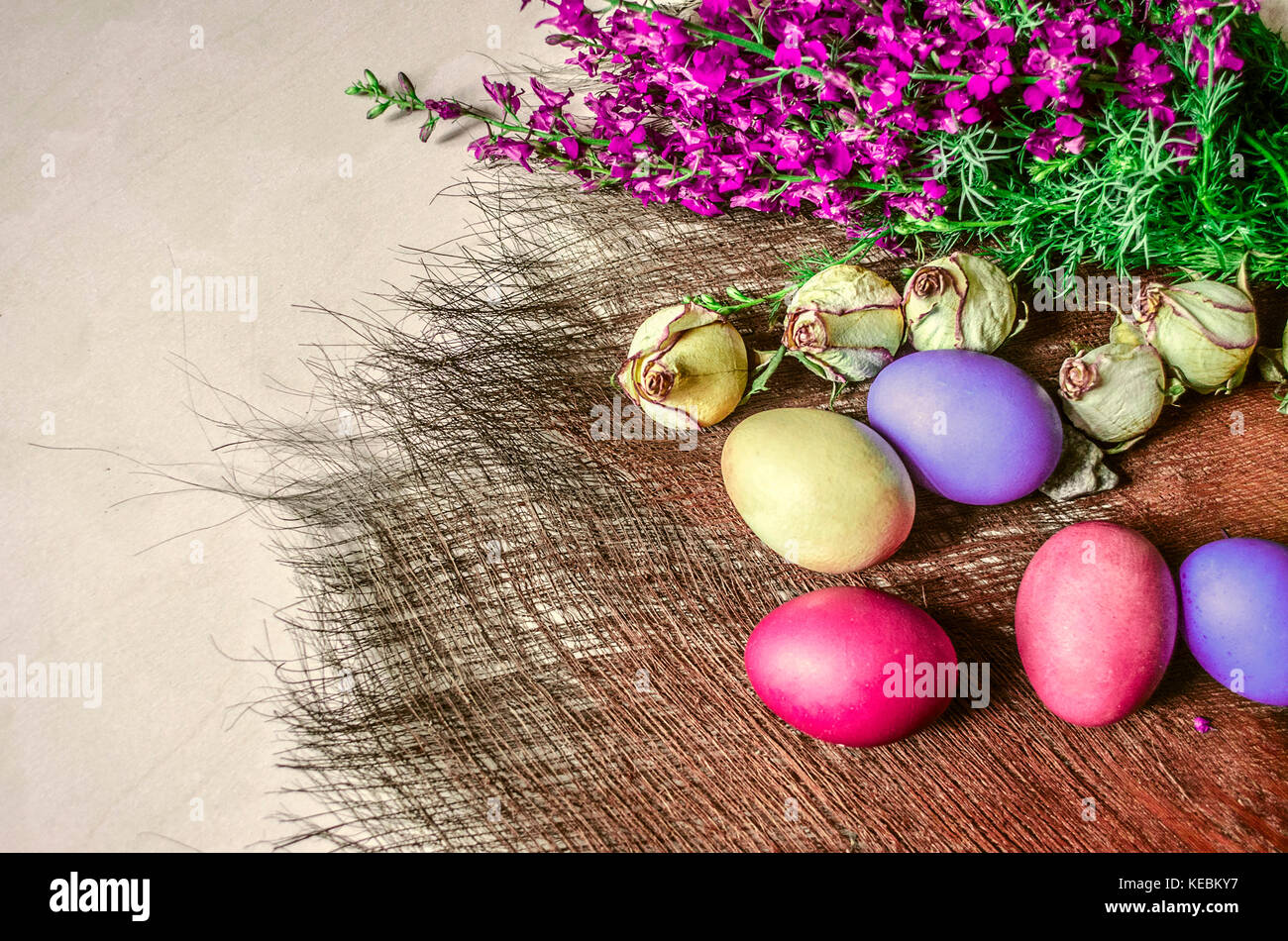 Huevos de pascua de colores brillantes cerca del ramo de flores silvestres y capullos secos de rosas en un subsuelo de paja Foto de stock