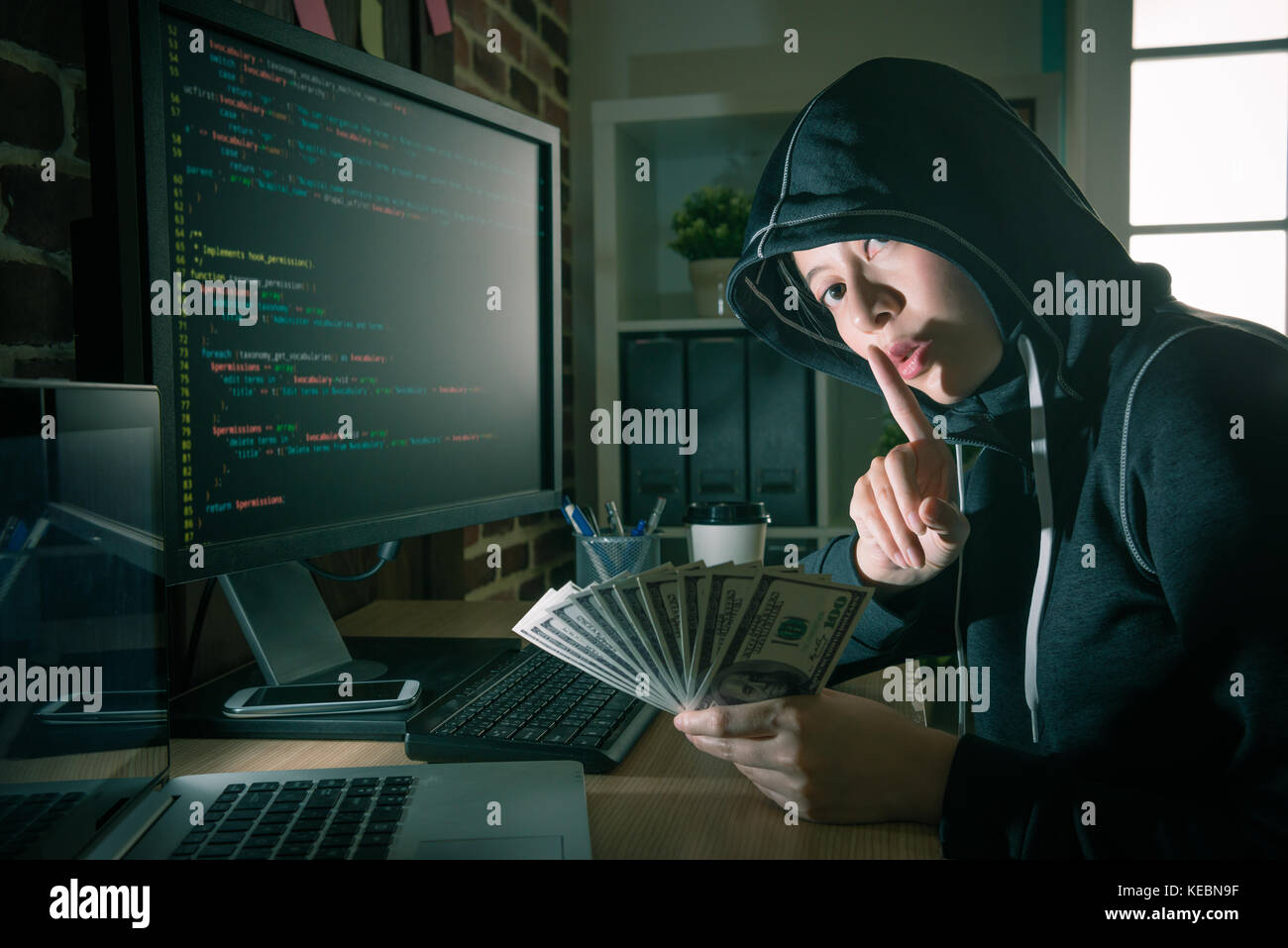 Jóvenes profesionales programador femenino utilizando código idioma sistema crímenes conseguir muchos billetes de dinero y mirando a la cámara haciendo gestos silenciosos. Foto de stock