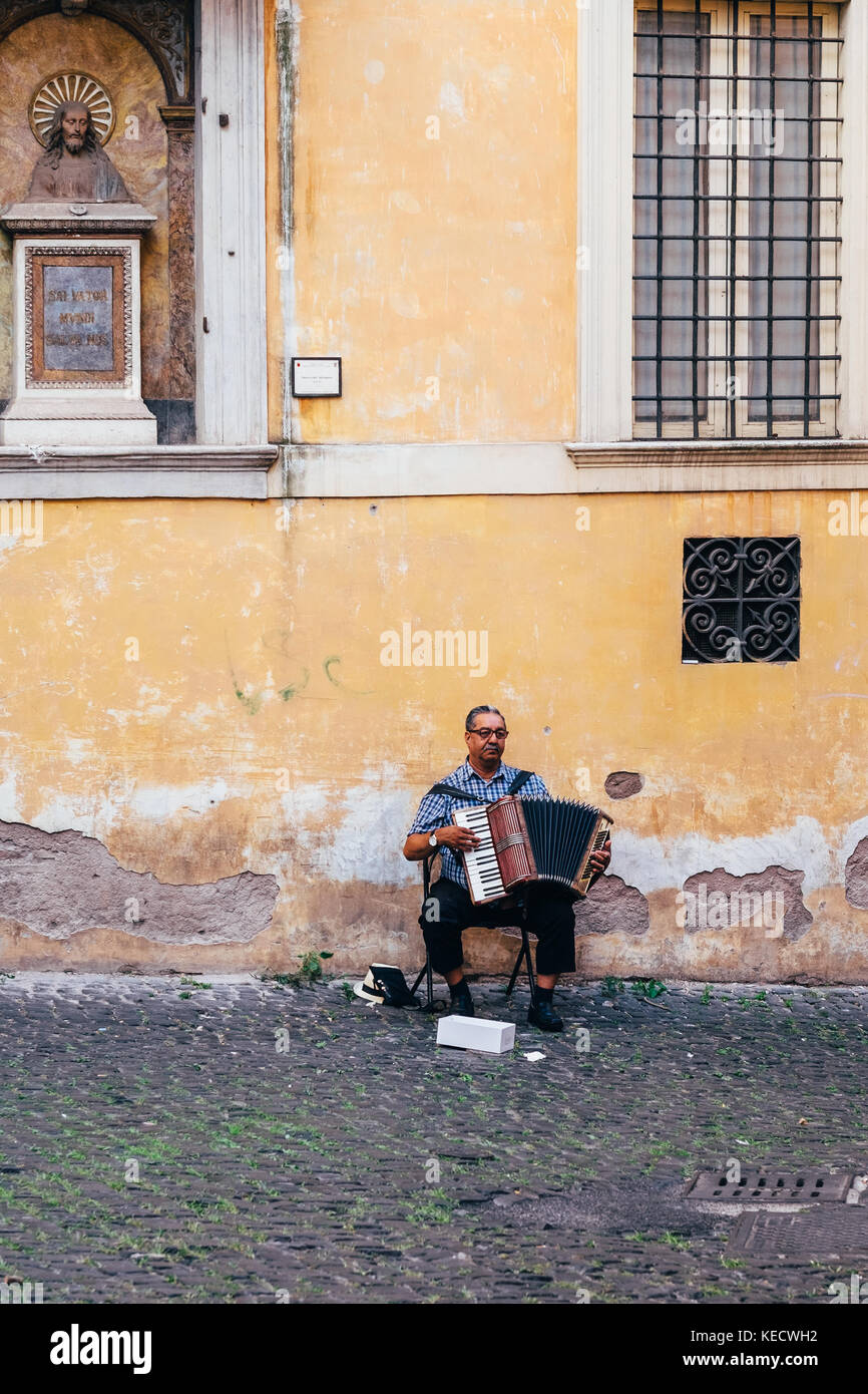 Un hombre toca el acordeón en el barrio del ghetto de Roma, Italia. Una estatua de Jesús mira hacia él. Foto de stock