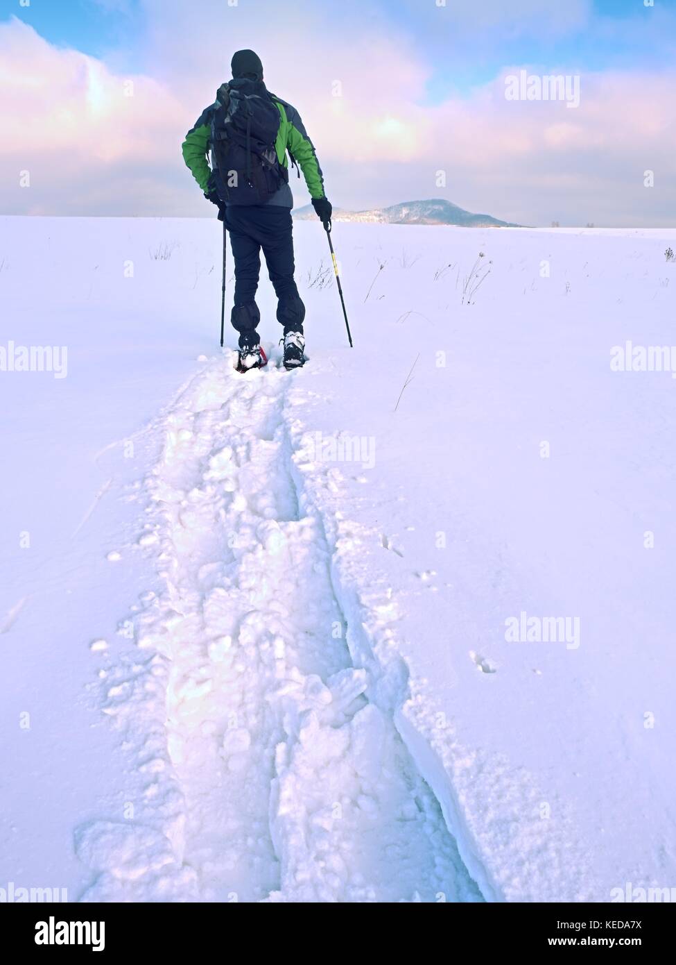 Excursionista con mochila raquetas de nieve profunda deriva. hombre caminar  con raquetas de nieve en la colina. caminante en verde chaqueta de invierno  gris y negro pantalón trekking snowsho Fotografía de stock -