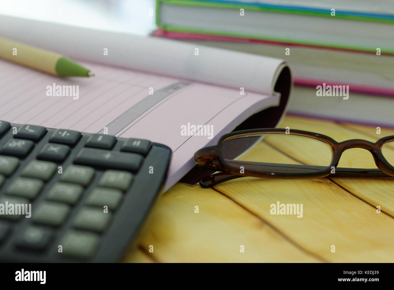 Calculadora,Gafas,pluma,recibo y factura y libro de libros apilados en el fondo. Foto de stock