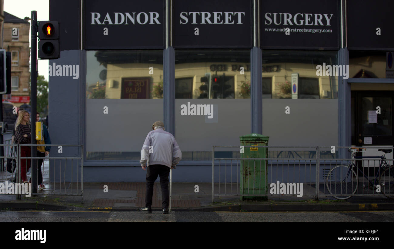 Senior Citizen hombre viejo pueblo en el centro de la ciudad de Glasgow radnor cirugía calle lucha para cruzar calles en el tiempo porque el tiempo de cruce peatonal bip Foto de stock