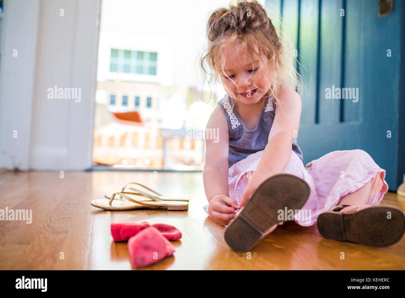 Chica caucásica sentada en el suelo que sujeta la sandalia Foto de stock