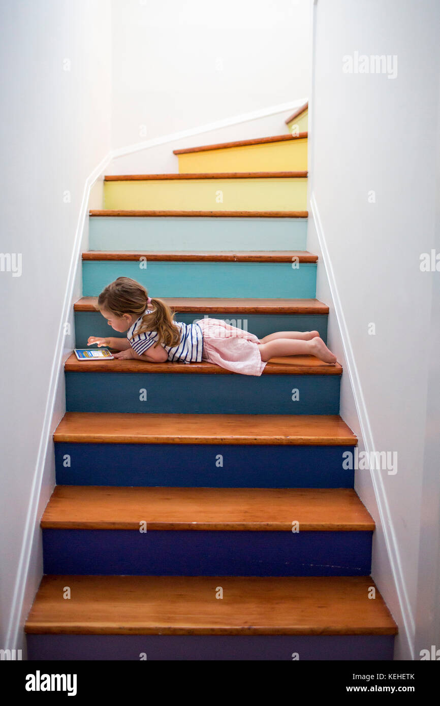 Chica caucásica usando una tableta digital en una escalera multicolor Foto de stock