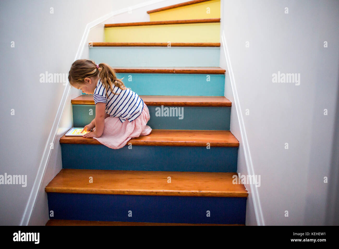 Chica caucásica usando una tableta digital en una escalera multicolor Foto de stock