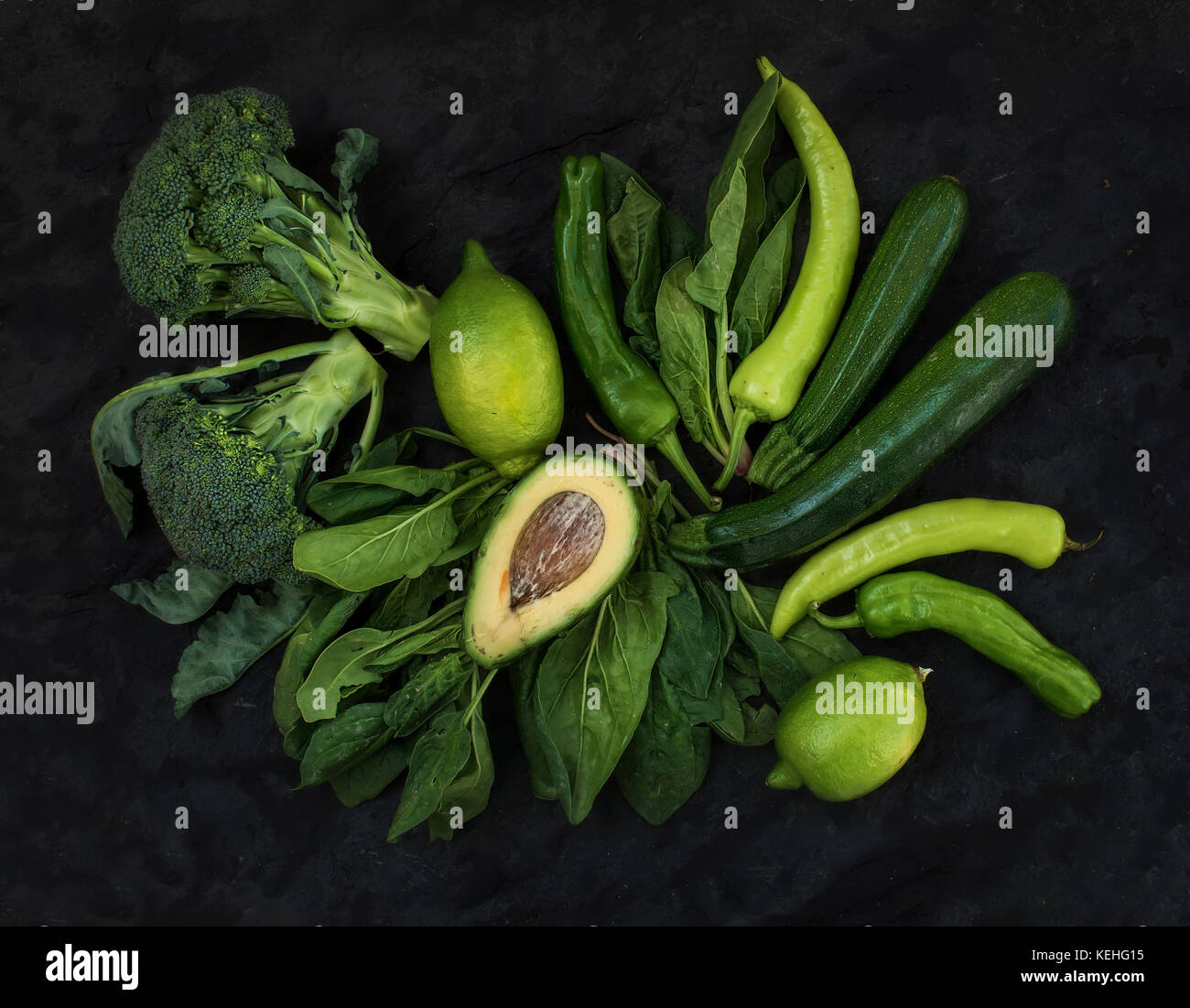 Materias vegetales verdes. El brócoli, aguacate, pimiento, espinacas, zuccini y cal sobre fondo de piedra oscura, vista superior Foto de stock