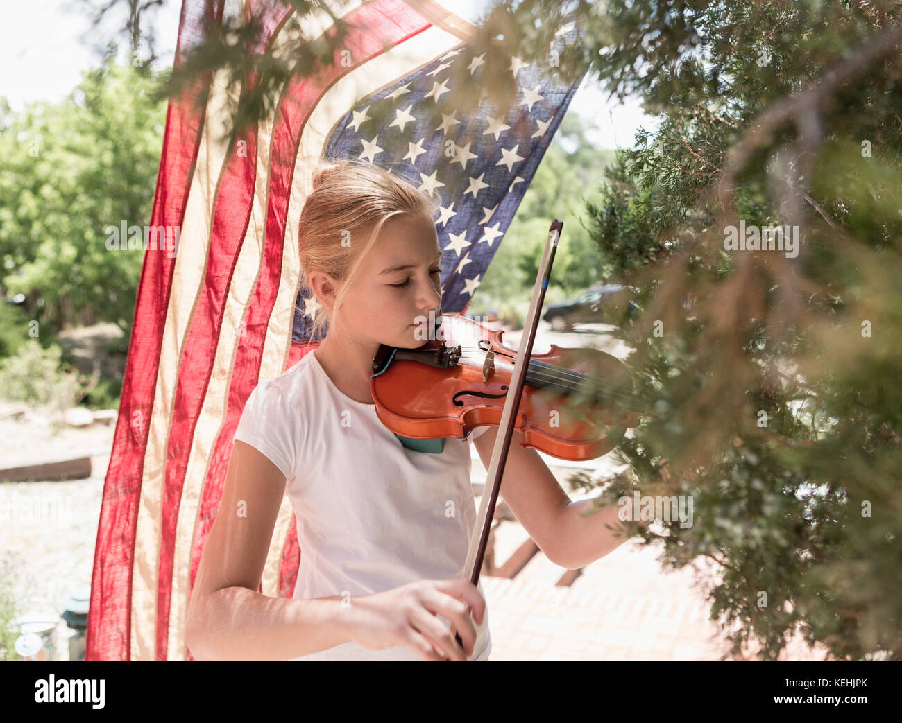 Niña caucásica tocando violín cerca de la bandera americana Foto de stock