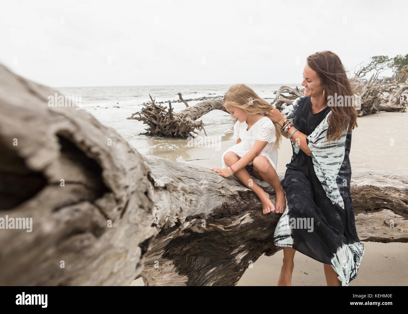 Madre e hija caucásica sentada sobre madera en la playa Foto de stock