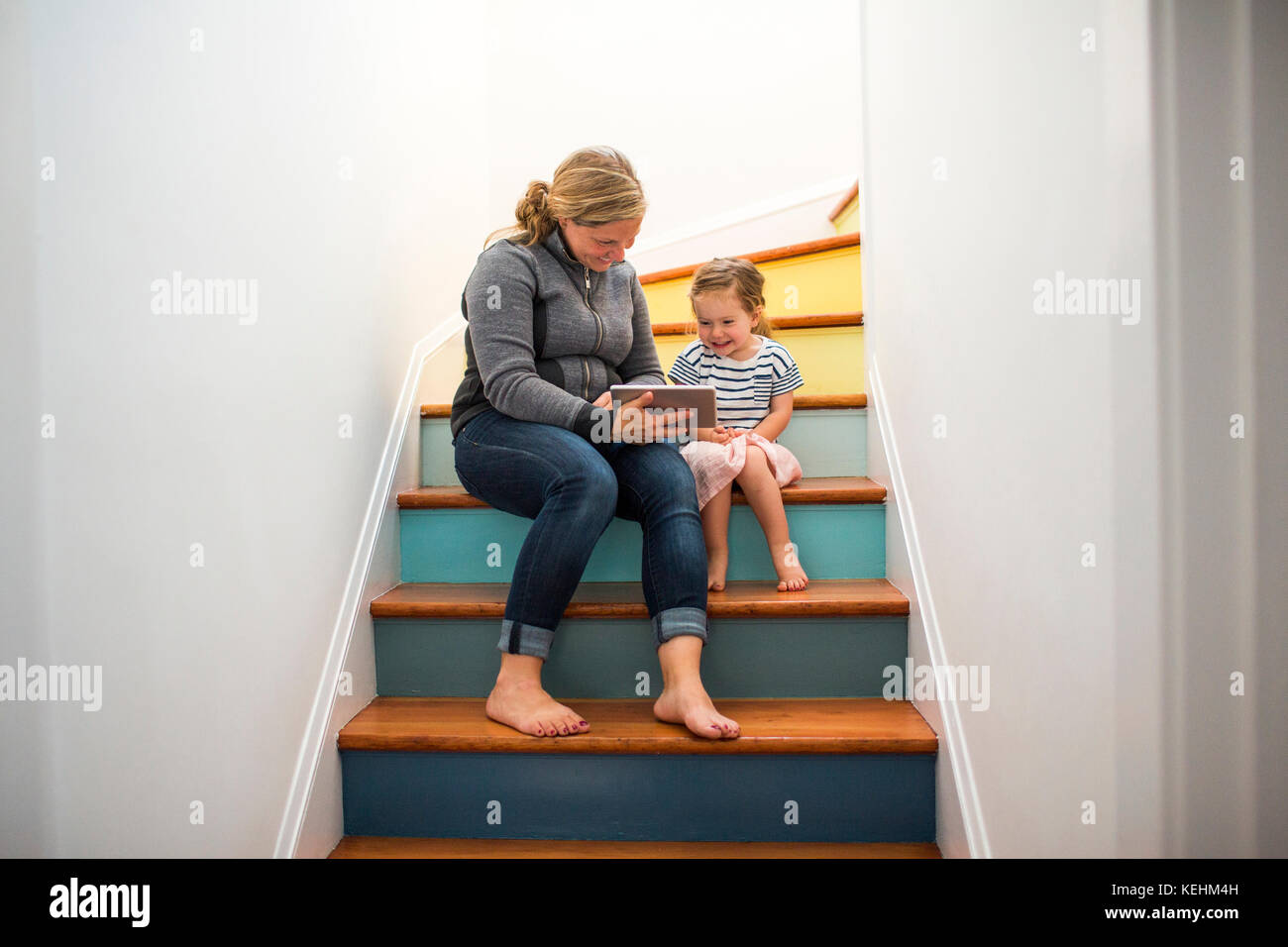 Madre e hija caucásica usando una tableta digital en la escalera Foto de stock