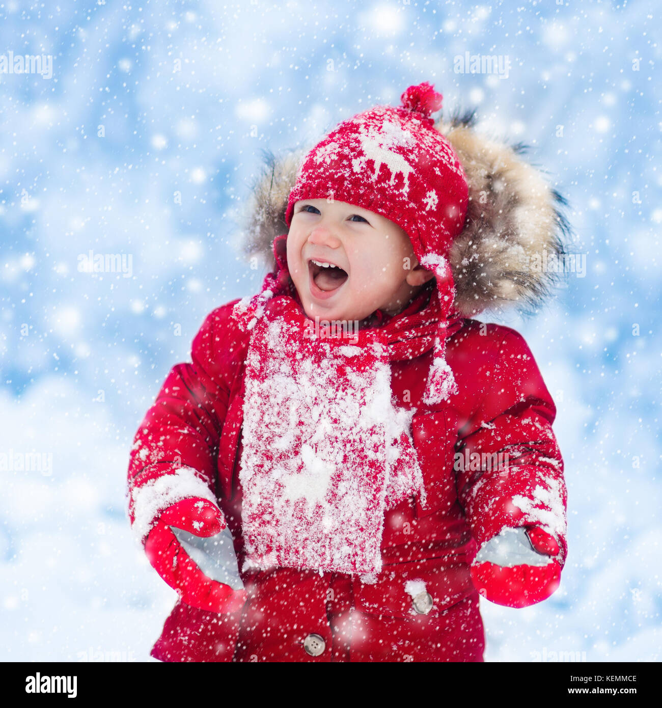 Bebé jugando con nieve en invierno. el pequeño niño chico en chaqueta roja  y gorro de punto de renos de navidad atrapar los copos de nieve en  invierno, parque infantil en navidad