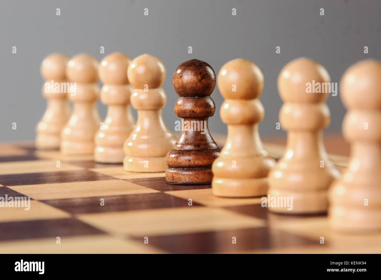 Un peón negro se encuentra en medio de una hilera de peones blancos, destacando sus diferentes características de la aceptación del grupo. Foto de stock