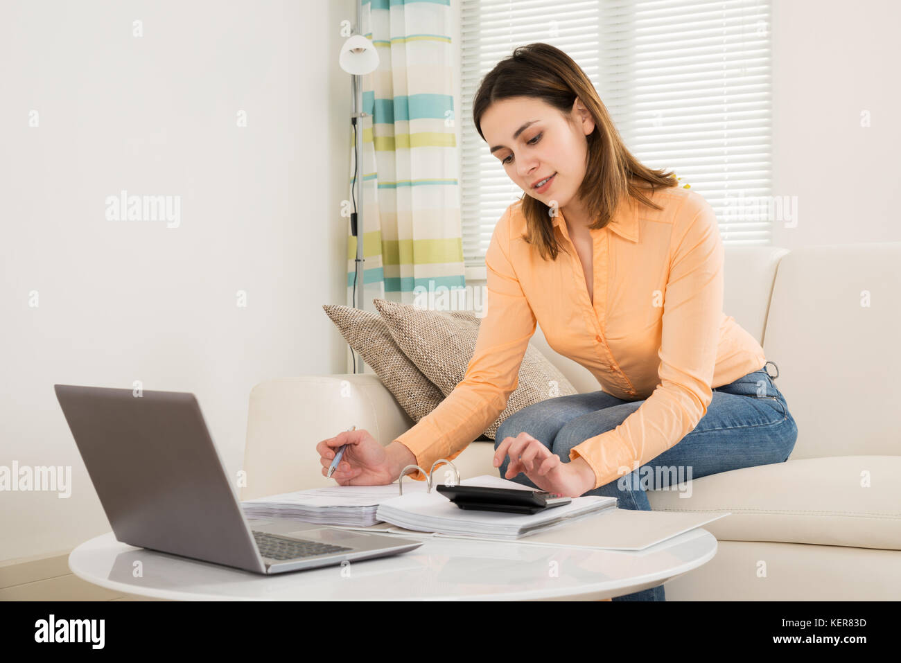 Mujer joven sentado en un sofá calcular las facturas en su habitación Foto de stock