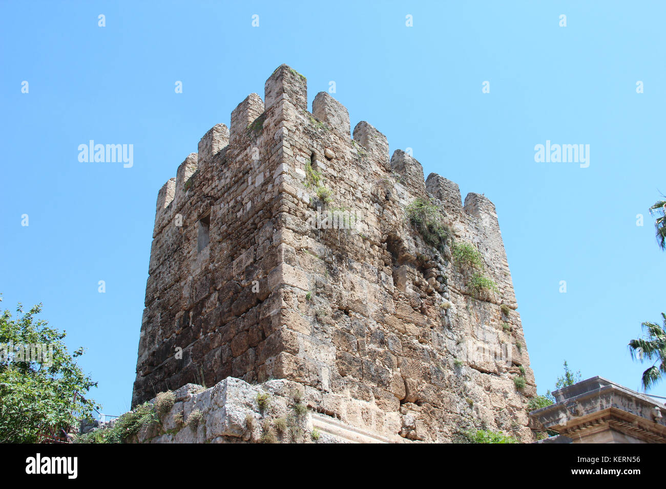 La antigua torre almenada en la antigua puerta de Adriano, en Antalya, Turquía. En el fondo de cielo azul y verde de los árboles. Foto de stock