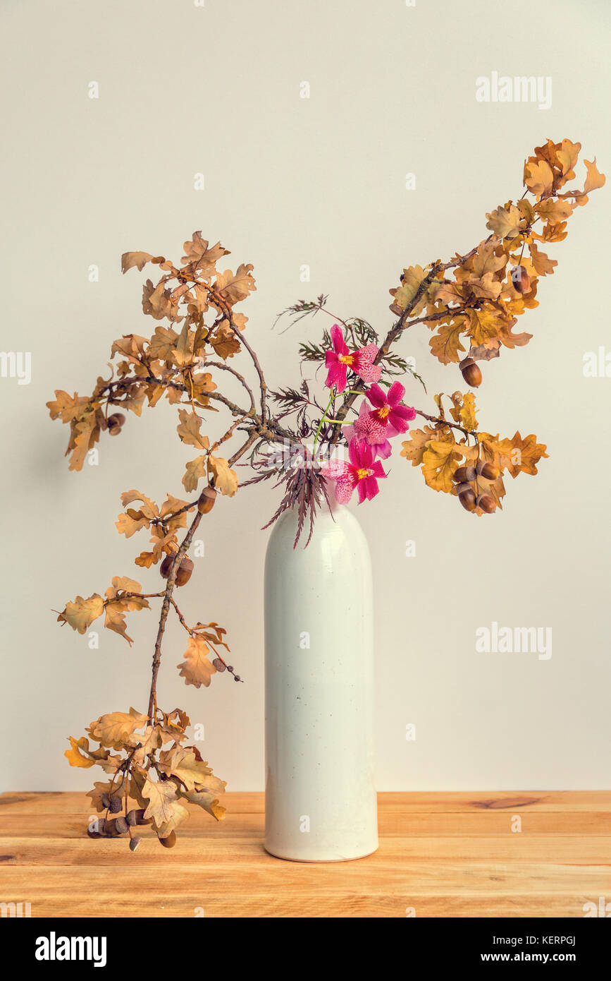 Otoñal ikebana (arreglo floral japonés) con ramas de árboles de roble y orquídeas en un florero Foto de stock