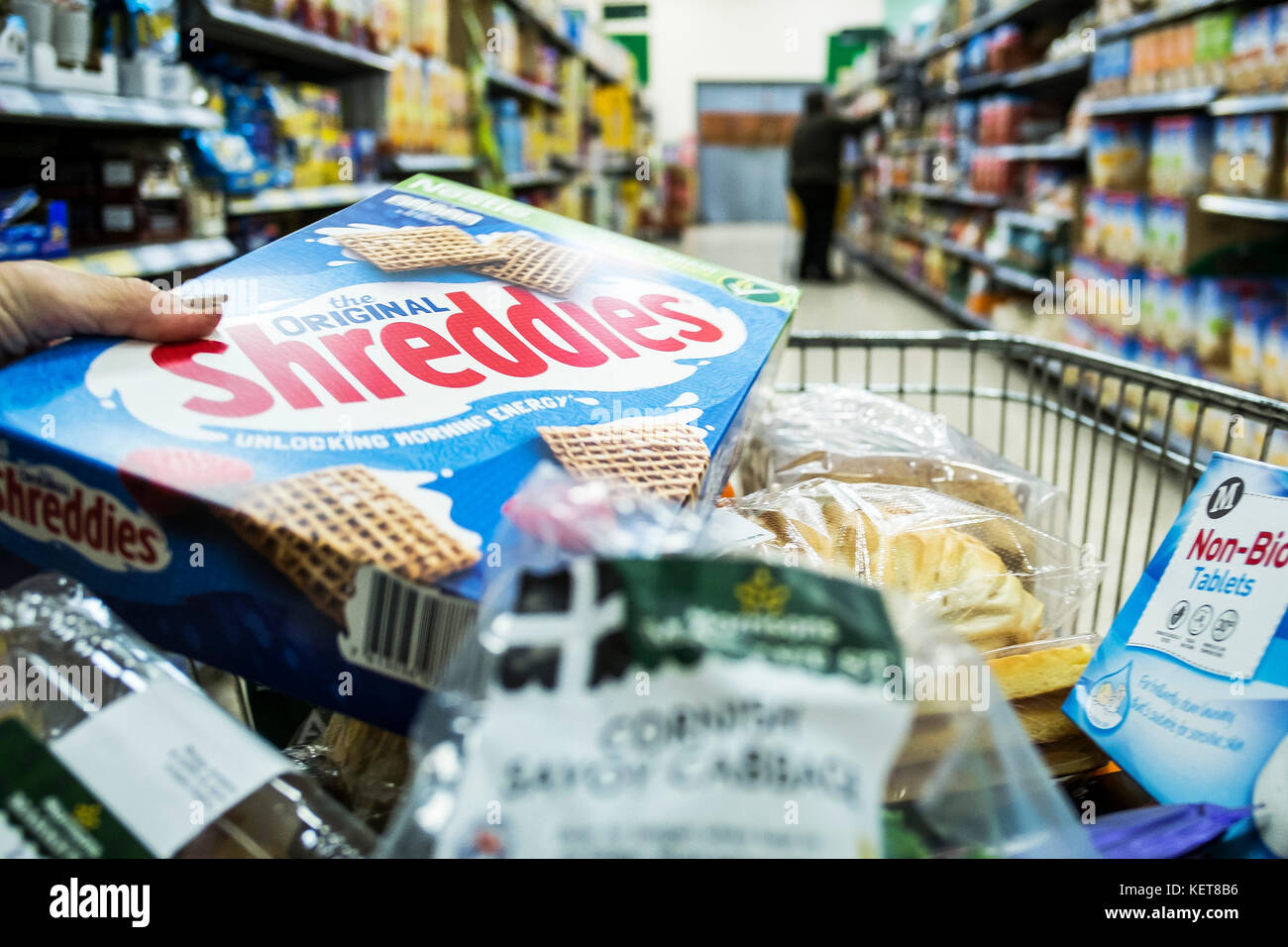 Ir de compras en un supermercado Morrison - un comprador poniendo una caja de cereal en un carrito de la compra. Foto de stock