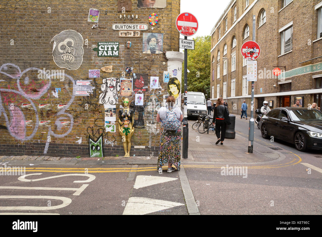 Mujer mirando una miríada de piezas de arte de la calle en la pared en el cruce de la calle Buxton y Brick Lane en Londres, Inglaterra Foto de stock