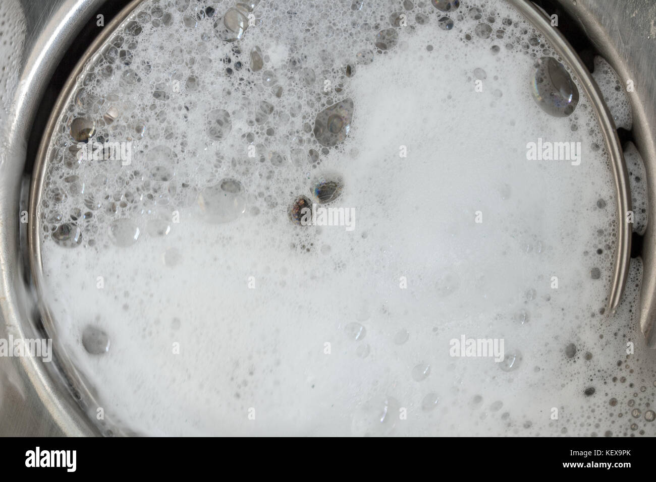 La blanca espuma con burbujas de cleane en un lavabo. Orificio de drenaje con burbujas de jabón en el fregadero de metal, macro vista. Ajustable mecánicamente el tapón de drenaje closeup. Foto de stock