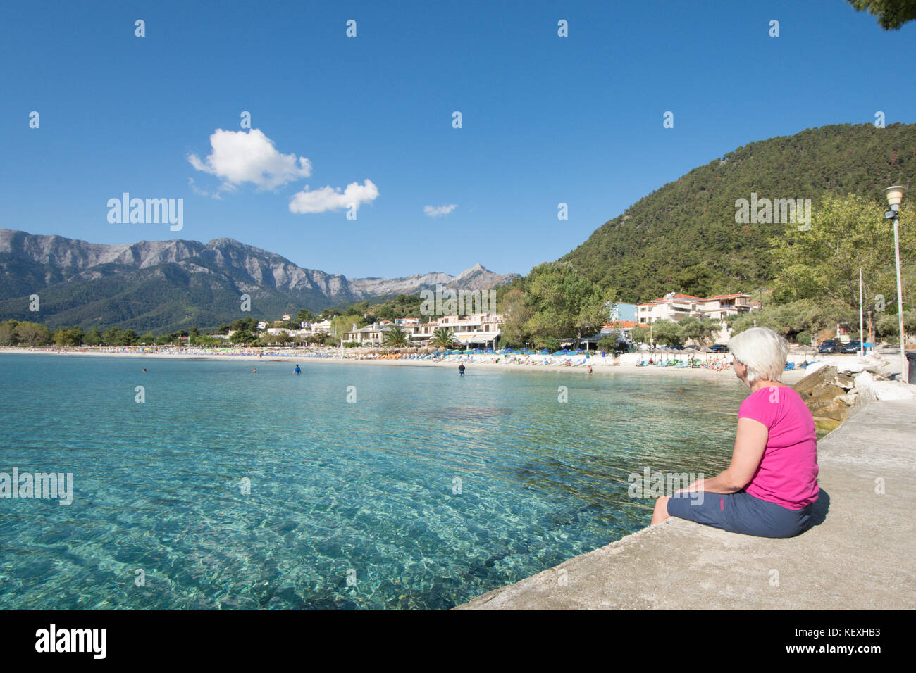 Mujer en el malecón mirando Golden Beach, Chrysi Ammoudia, Thassos, Grecia, isla Griega, montañas, Ypsarion Ipsarion montaña. Septiembre 2017 Foto de stock