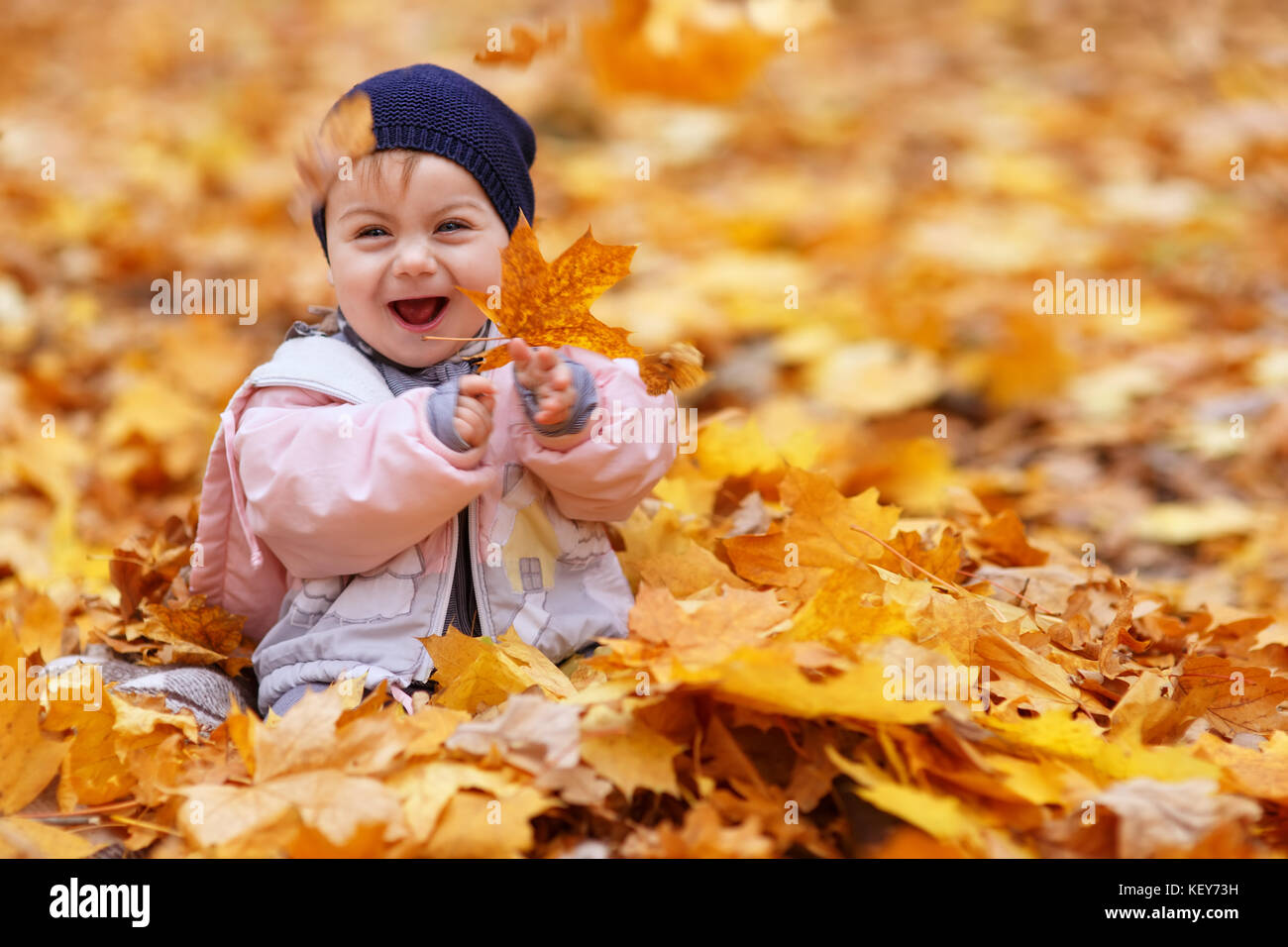 Niña riendo y jugando con hojas doradas Foto de stock