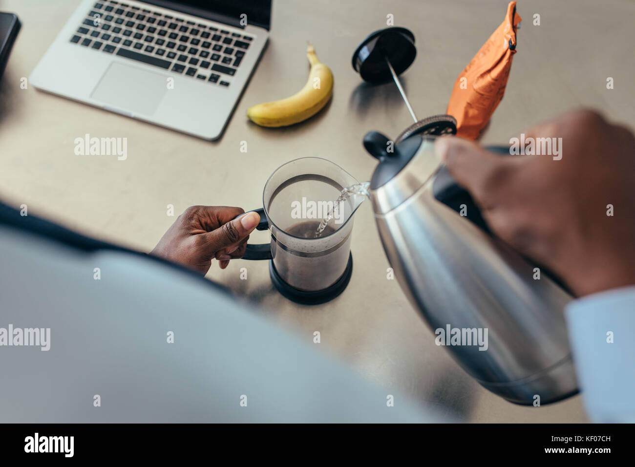 Hombre vertiendo agua caliente en la cafetera. Hombre preparar café en la  mesa de desayuno con un ordenador portátil al lado Fotografía de stock -  Alamy
