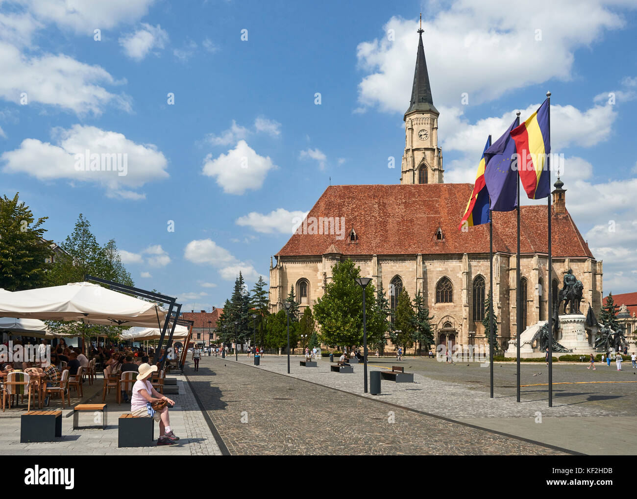 Iglesia de San Miguel y la Plaza Unirii en Cluj - con Linda sentado en la banqueta pública y cafeterías en primer plano Foto de stock