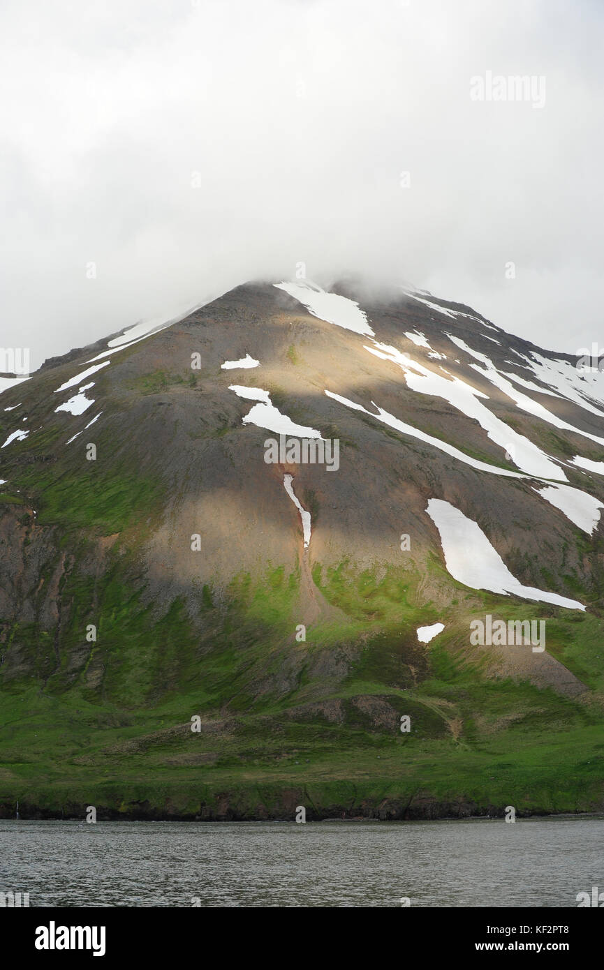 Parches de nieve y pasto verde en la montaña con cielo nublado en Siglufjörður Anuncios, al norte de Islandia, Escandinavia Foto de stock