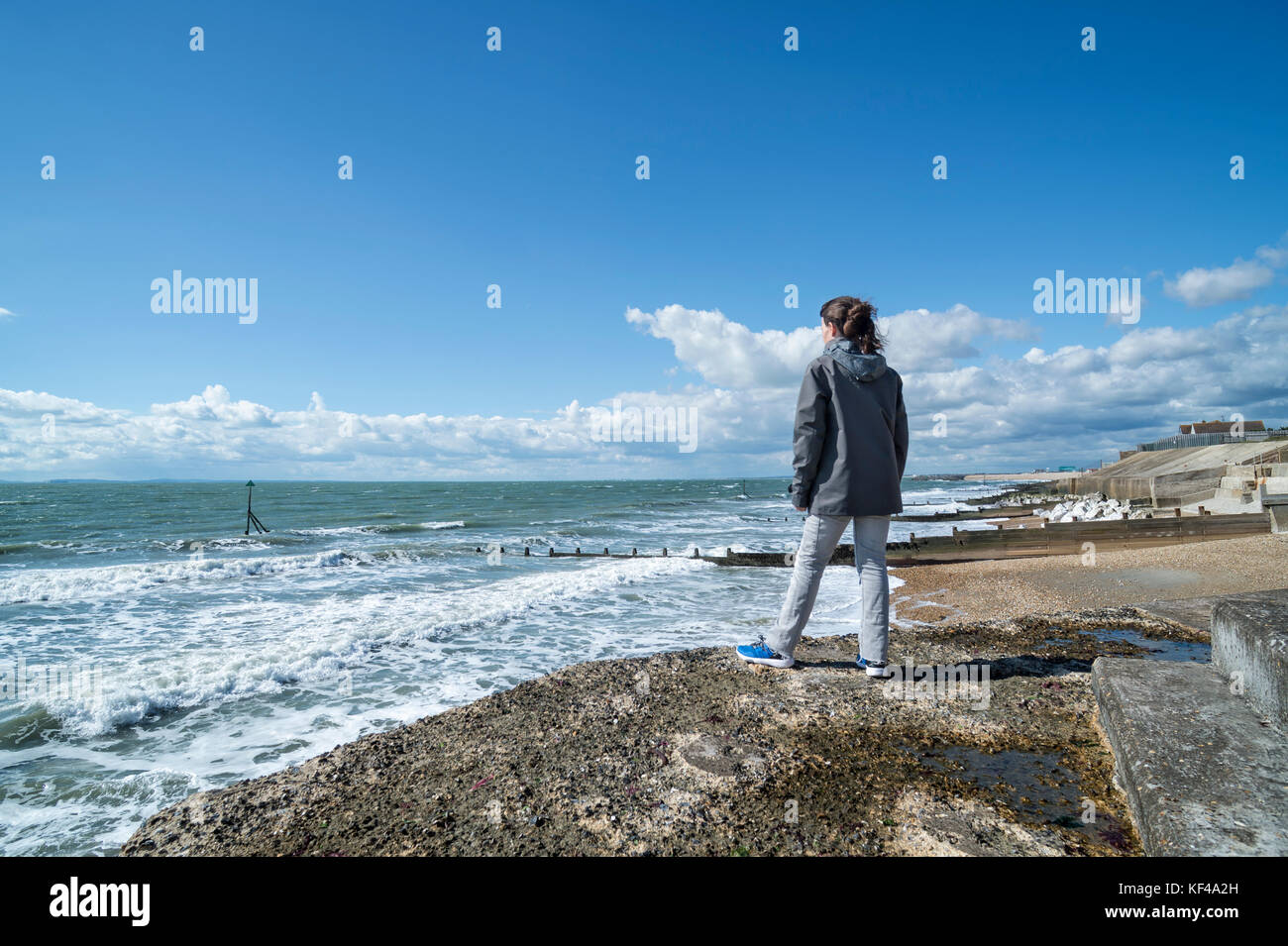 Mujer de pie sobre un rompeolas mirando al océano. Foto de stock