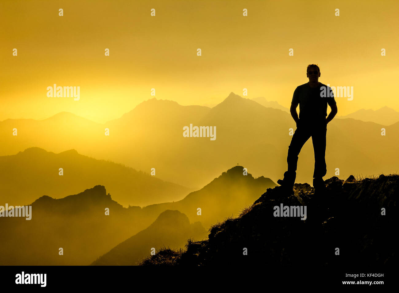 Hombre de pie en la cumbre disfrutando del amanecer y la espectacular cordillera capas siluetas. Foto de stock