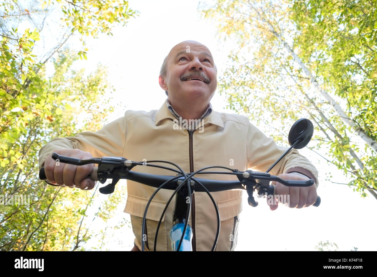 Senior hombre caucásico en paseo en bicicleta en el campo. Árboles verdes en el fondo. Él es feliz y activo. Foto de stock