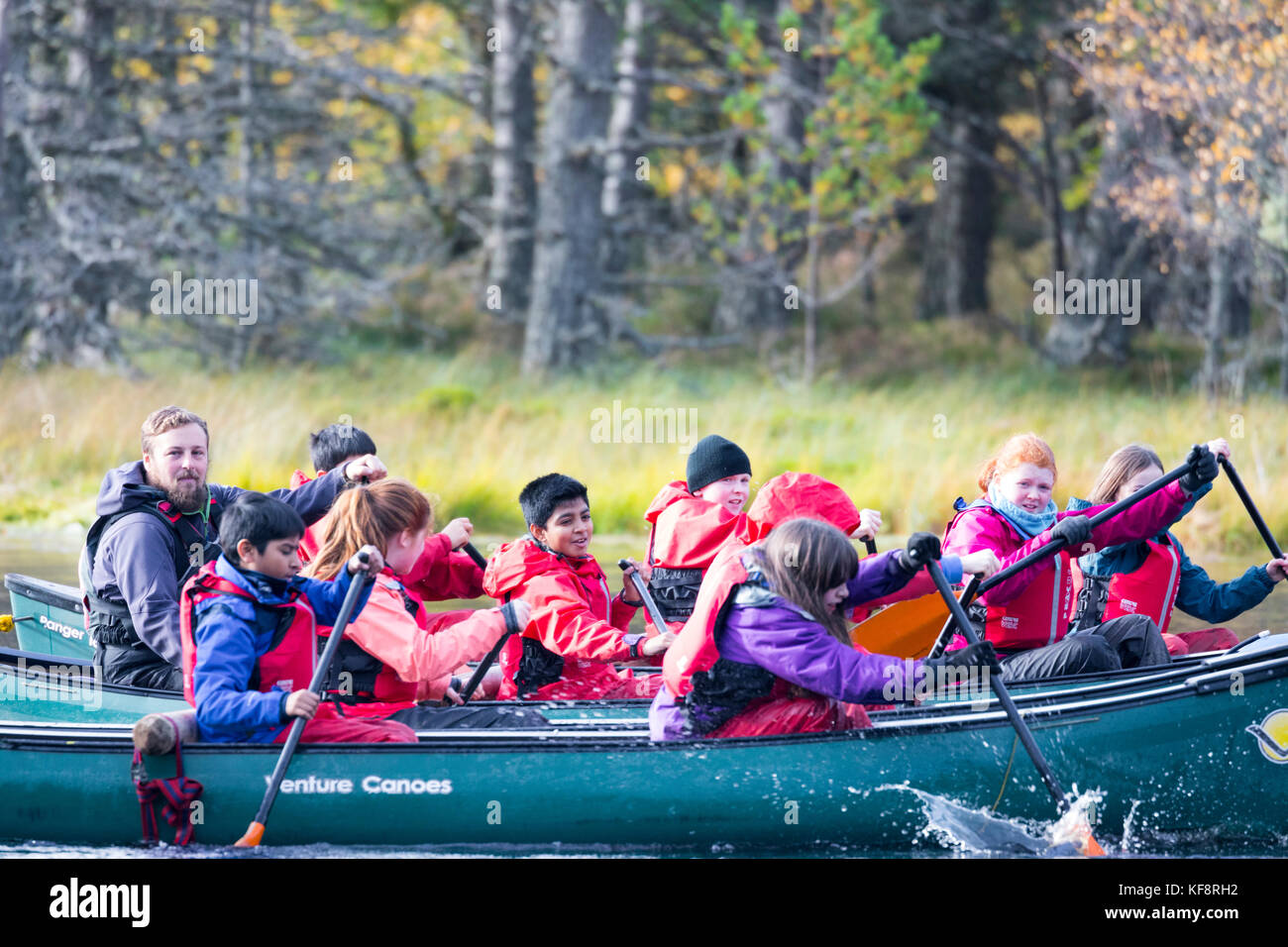 La escuela los niños que disfrutan de los deportes de aventura sobre Lochan Uath con su instructor en otoño entre los Inshriach bosque en las Tierras Altas de Escocia, Reino Unido Foto de stock
