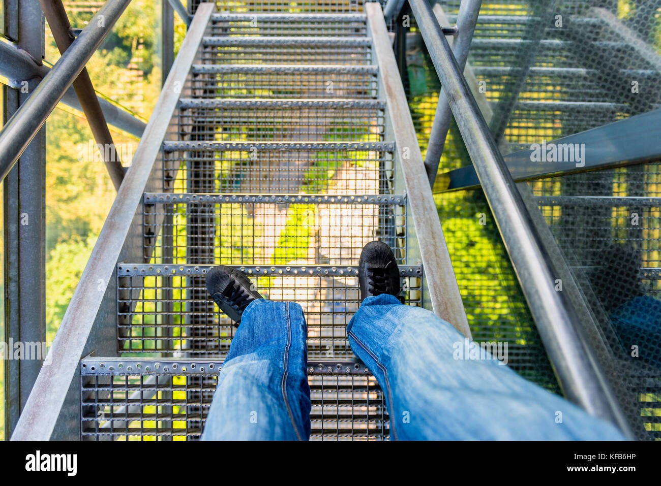 Vista en primera persona de las piernas y pies masculinos en la escalera exterior de alta altitud, mirando hacia abajo y con enfoque selectivo Foto de stock