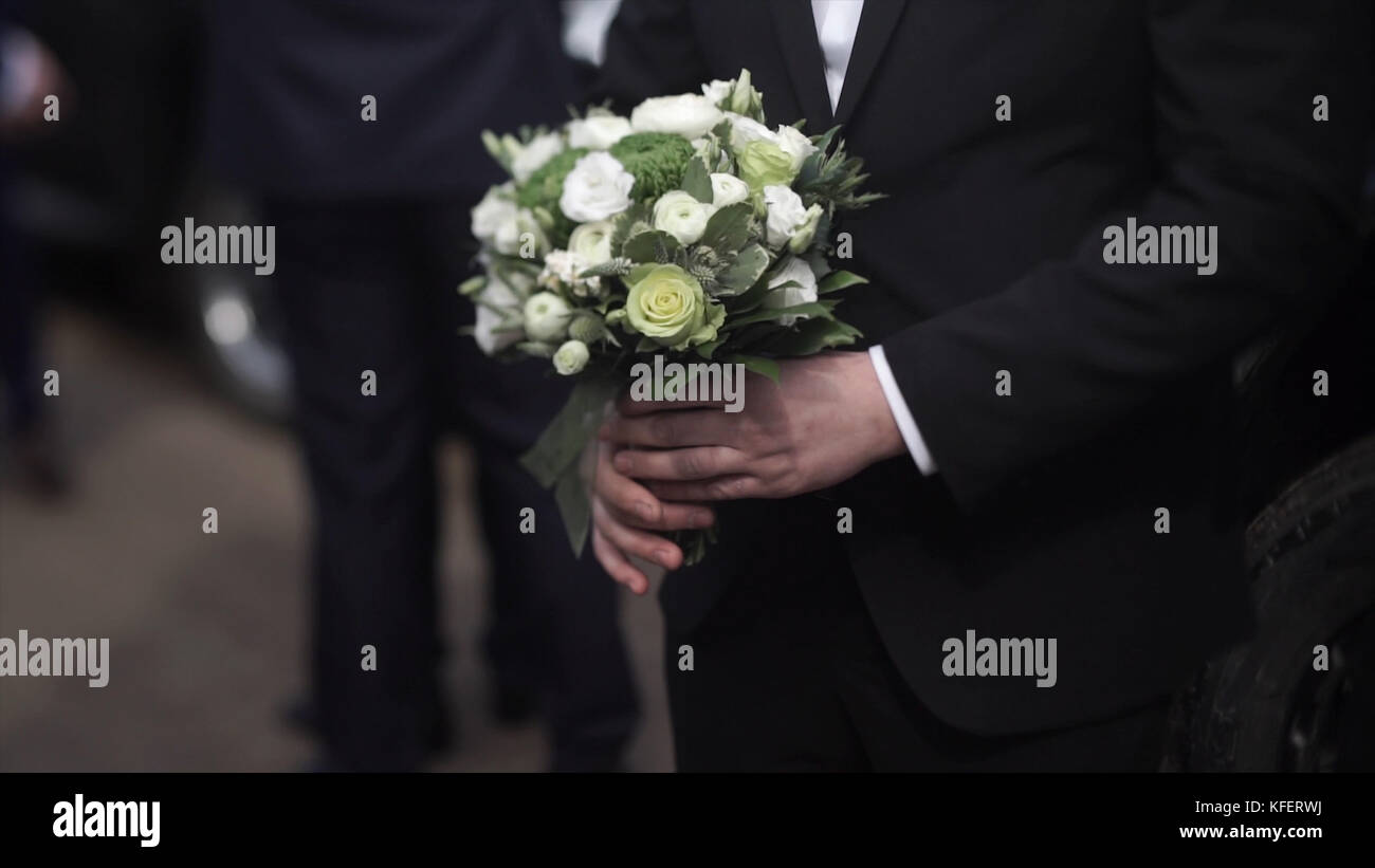 Guapo empresario sosteniendo flores. El novio en un traje sosteniendo un  ramo de flores, un arreglo floral para la solapa del novio. hombre elegante  boda vestido con un moderno traje negro y