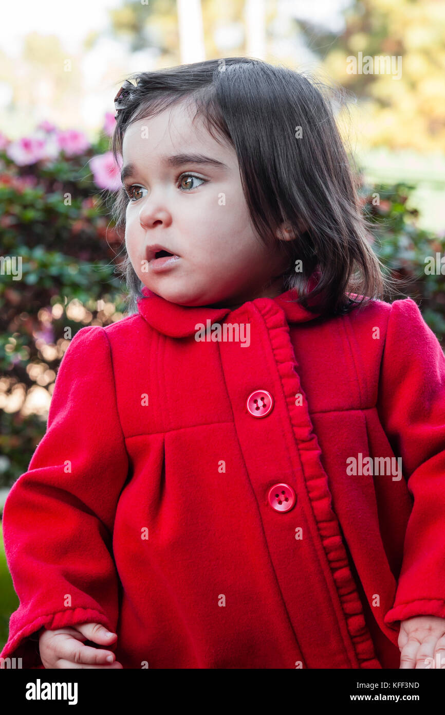 Lindo, bonito, feliz y moda bebé niño niña, vestida con un buen abrigo  largo rojo de moda o abrigo en el frío día de invierno en un jardín. 18  meses Fotografía de