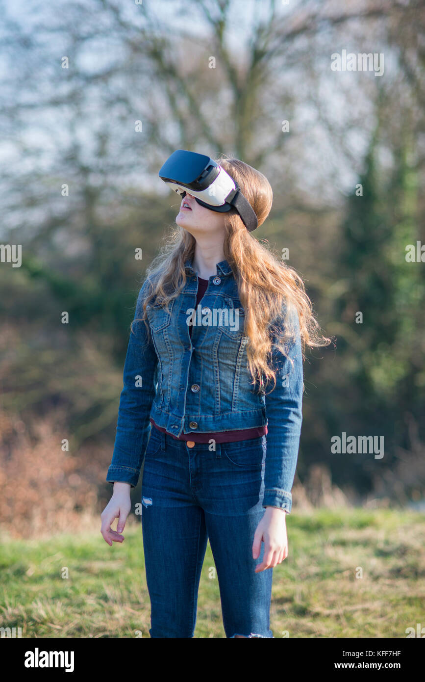 Adolescente vestida de denim en sunshine llevar casco de realidad virtual en el exterior Foto de stock