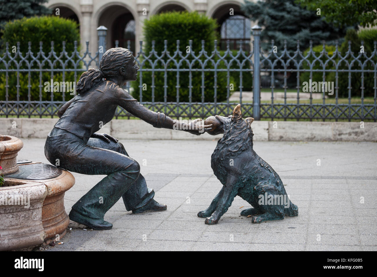 Chica con su perro, calle escultura en bronce, Plaza Vigado, ciudad de Budapest, Hungría, niña jugando con el animal con la bola en su boca Foto de stock