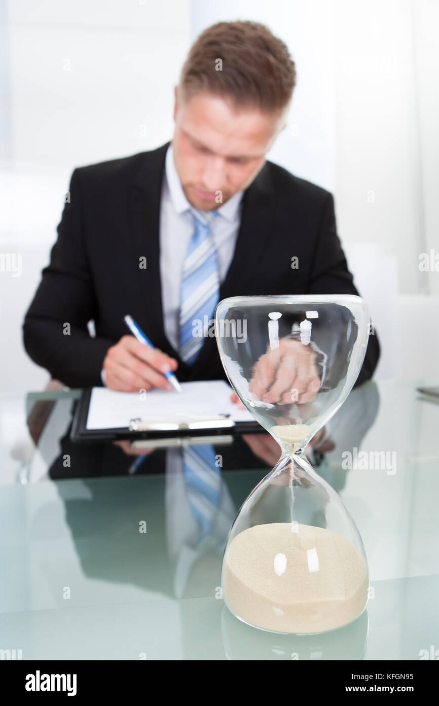 Empresario de completar el documento con un reloj de arena en la mesa delante de él Foto de stock