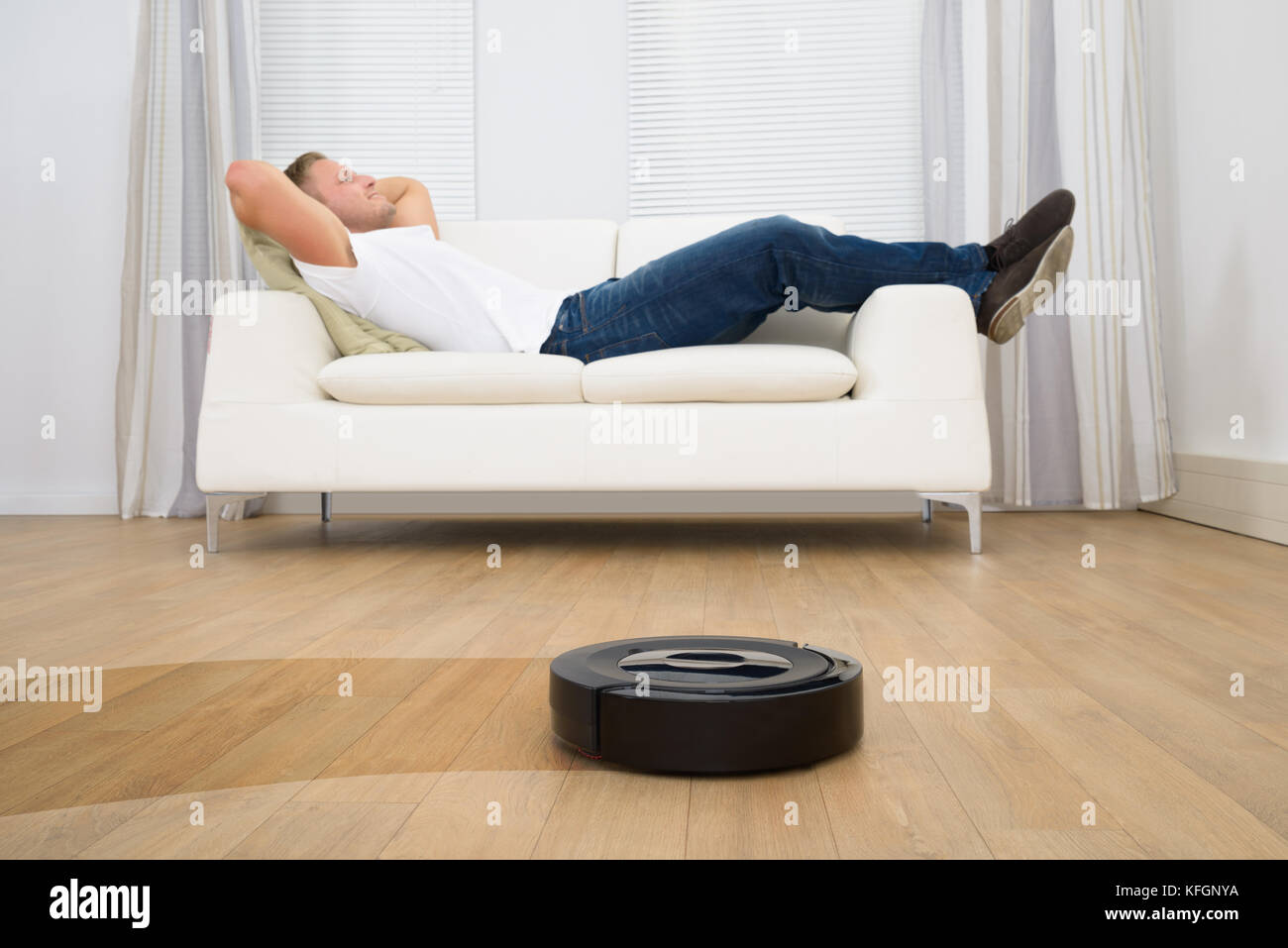 El hombre en el sofá relajante con aspirador robótico sobre piso
