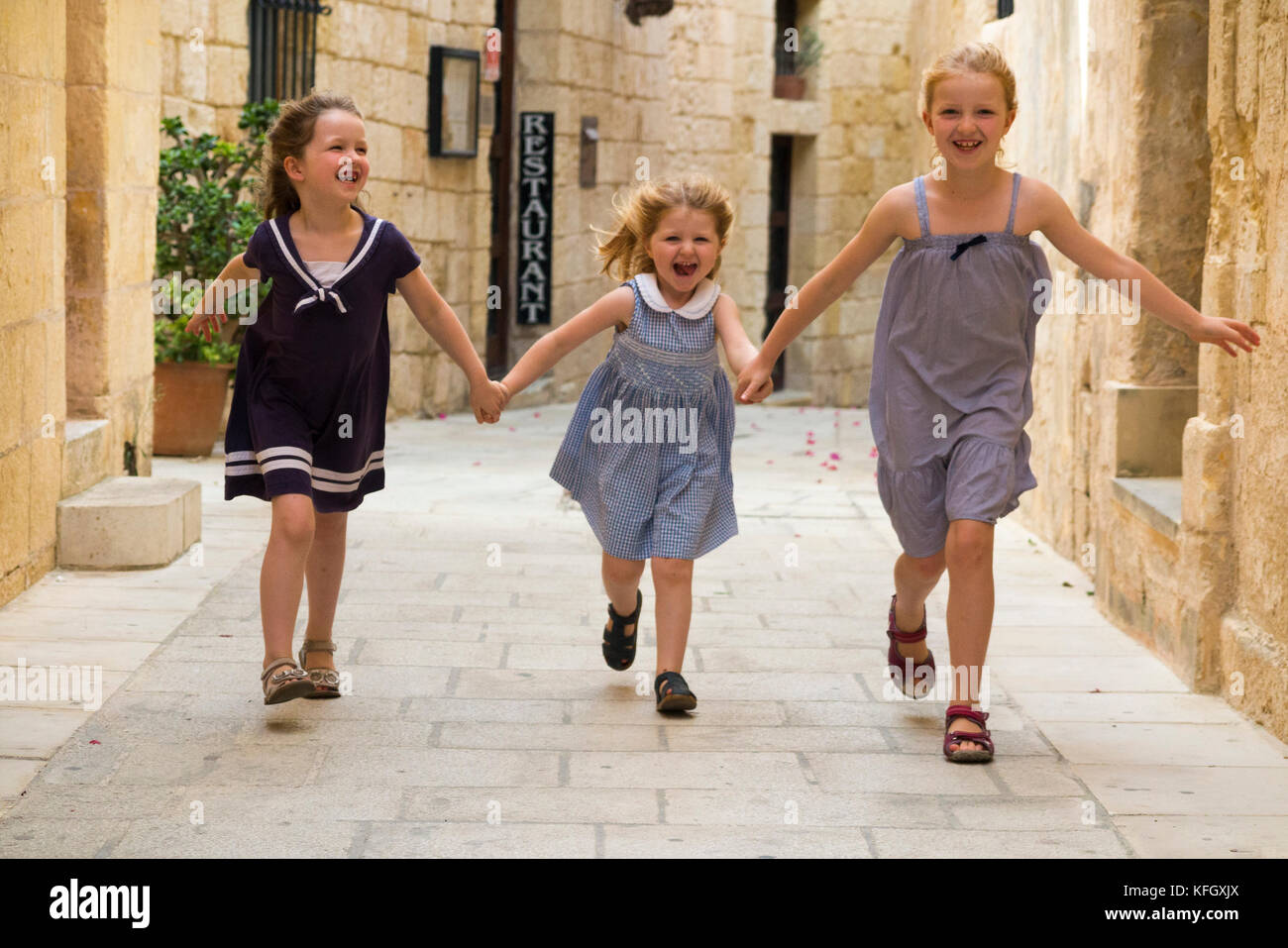 Tres jóvenes hermanas / niñas / Niños / kids / kid entre 7, 3 y 5 años de edad, en una familia de vacaciones, run & play y abarcan una calle angosta en Mdina, Malta Foto de stock